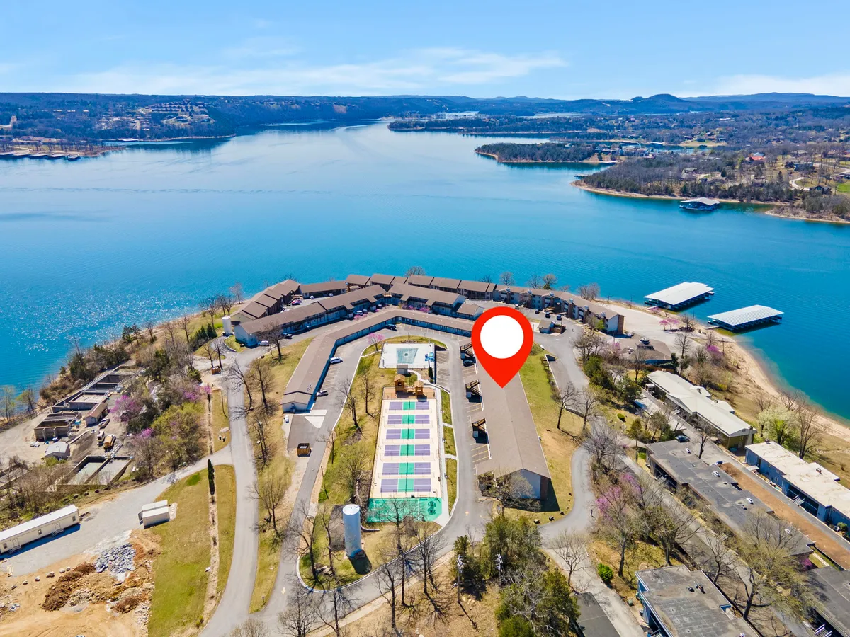 An inviting wide-angle exterior view showcasing the swimming pool, shimmering lake, and the surrounding resort landscape. Residential buildings are visible, with spaces for relaxing, swimming, and enjoying nature, all beneath a picturesque sky.