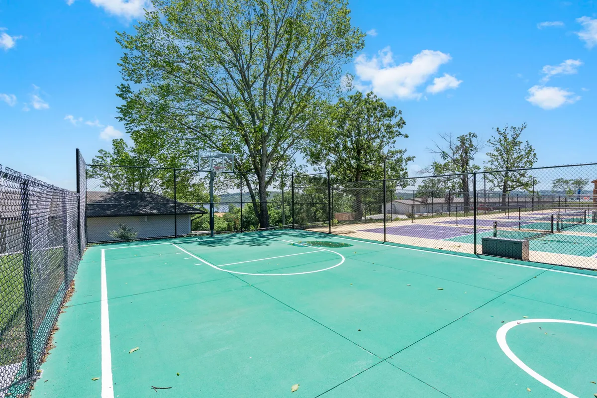 A fenced basketball court nestled among trees, perfect for friendly games and casual exercise. The playful mood encourages socializing and active competition within a safe, community setting.