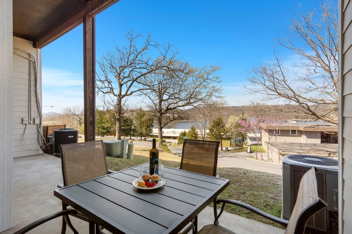 A picturesque outdoor dining table set with wine and fruit, overlooking a serene view of the lake from the patio. The setting is tranquil and encourages outdoor living, morning coffee, or evening relaxation under the stars.