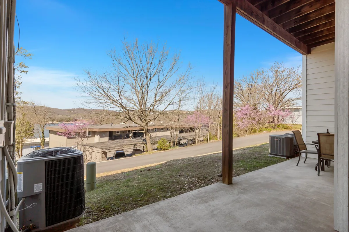 A peaceful patio area is shown with attractive landscaping, blossoming trees, and a view of distant hills. There are seating options for relaxing or socializing outdoors, and the space exudes tranquility and opportunity for morning coffee or evening drinks.