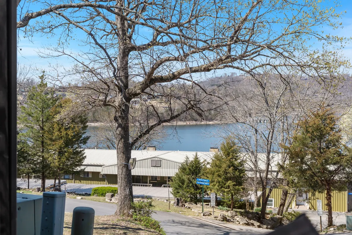 A peaceful view of Table Rock Lake framed by bare tree branches, small lakeside buildings, and surrounding natural greenery. The distance provides a sense of tranquility, making it ideal for nature walks, photography, or simply unwinding by the water.
