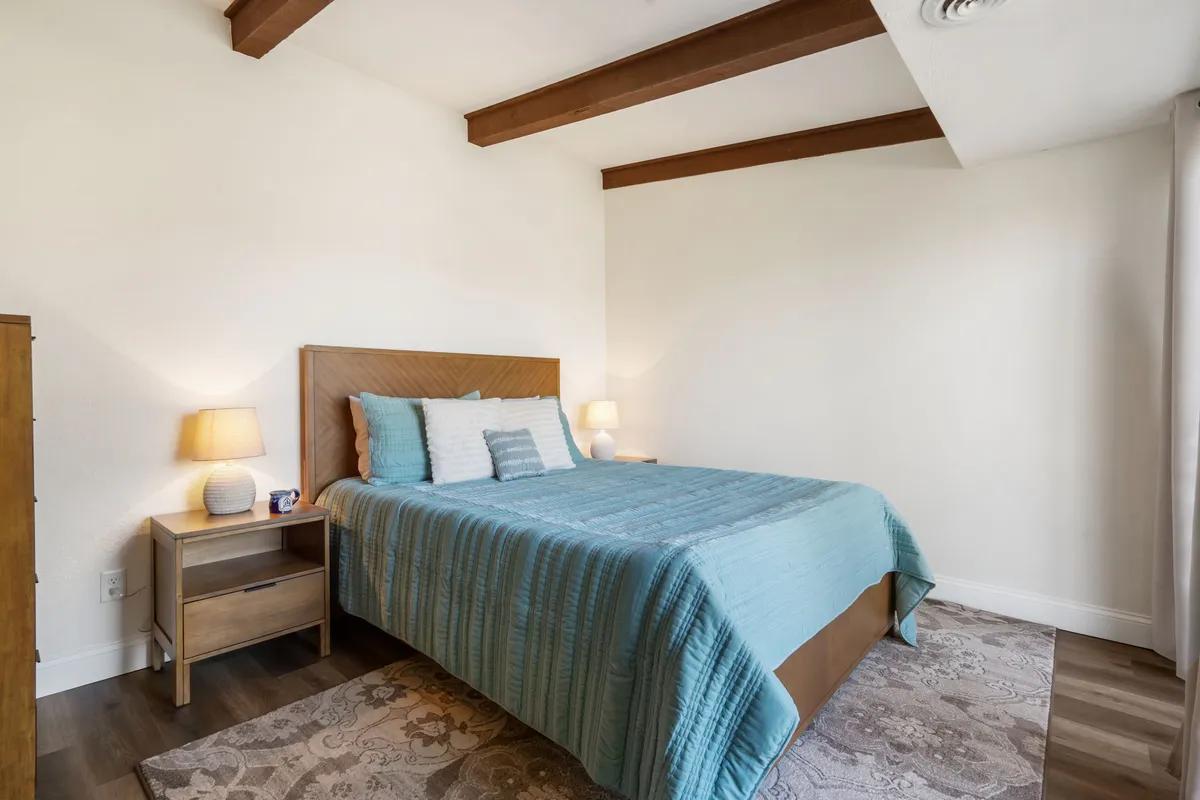 A serene bedroom scene featuring a large bed with crisp linens, a nightstand and lamp, and a cozy rug underfoot. The lighting is soft, evoking a tranquil mood perfect for rest and relaxation.