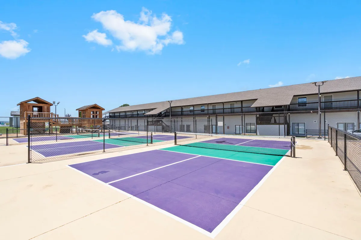 A vibrant exterior shot of well-maintained tennis courts with colorful surfaces, surrounded by resort buildings. The environment is energetic and invites friendly matches or group tournaments, with a clear sense of community and fun.