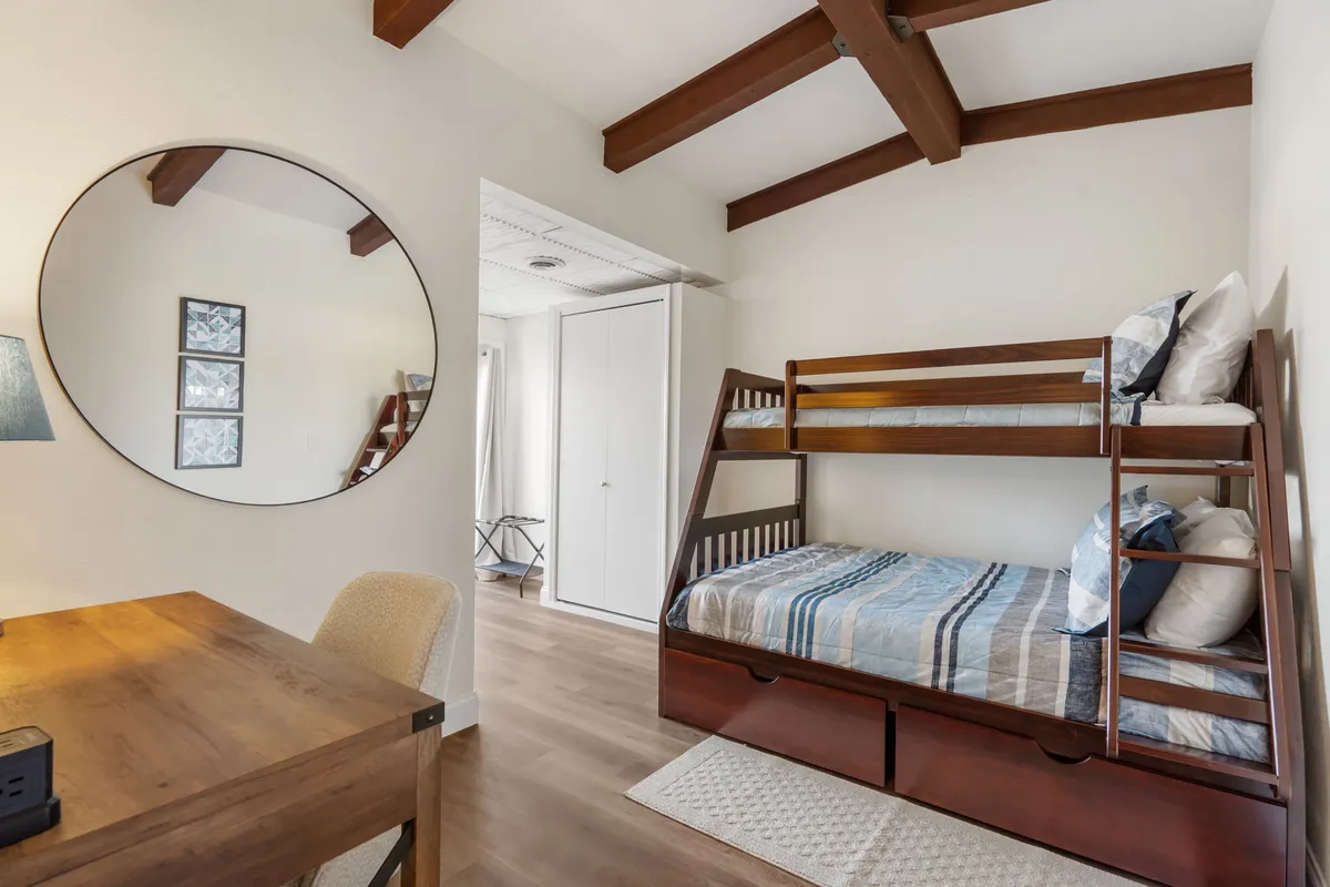A cozy bunk room showcasing a twin-over-full bunk bed, complemented by a round mirror and wooden desk. The compact but well-appointed space is comfortable, inviting, and ideal for children or friends.