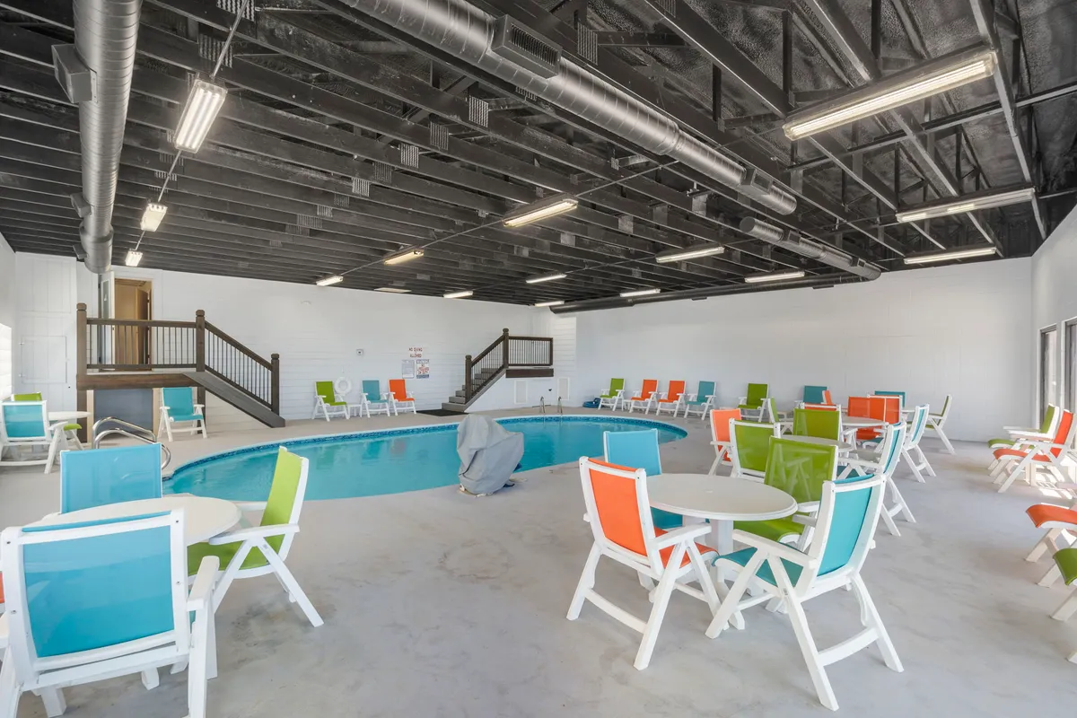 A bright and welcoming indoor pool area with colorful lounge chairs and tables set around the pool. Ample natural light filters in, creating a playful yet relaxing environment perfect for year-round swims and cozy moments together.