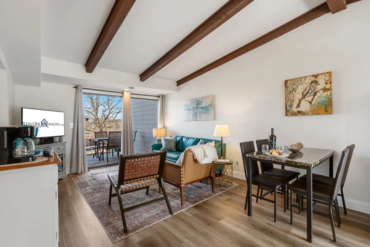 A welcoming angle of the living space showcasing a plush sofa, a dining table set for mealtime, a wall-mounted TV, and artwork that adds a homely touch. The layout emphasizes the flow between relaxation and dining activities.