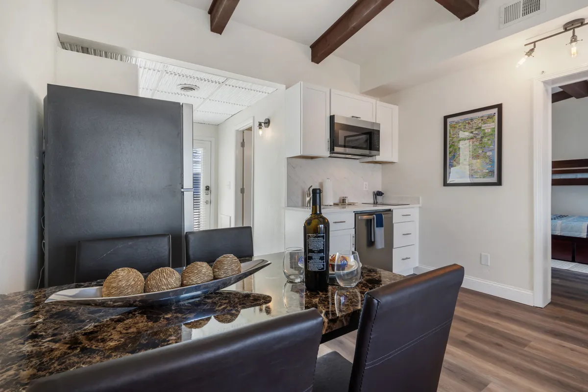 A welcoming dining area with a central table set for a meal, a bottle of wine, and a decorative bowl. The kitchen area is visible in the background, emphasizing the connection between meal prep and dining. The cozy setting encourages communal dining and celebrations.