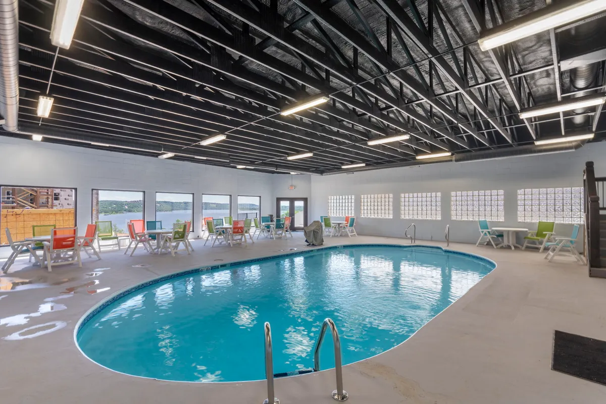 A spacious, well-lit indoor swimming pool area featuring colorful lounge chairs and large windows providing views of the outdoors. The inviting atmosphere is lively yet relaxing, with plenty of space for swimming, sunbathing indoors, and gathering with friends or family.